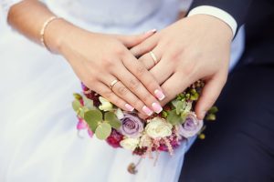 Hands,Of,Bride,And,Groom,With,Rings,On,Wedding,Bouquet.